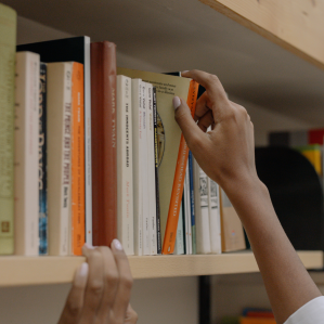 hand reaching for a book on a library shelf