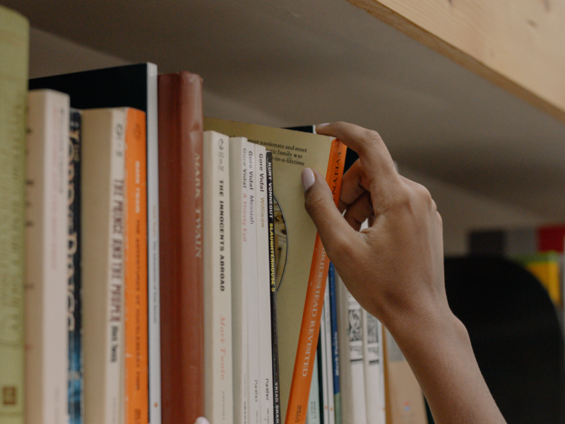 hand reaching for a book on a library shelf