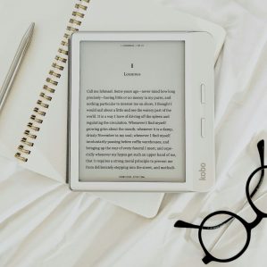 e-reader on top of a notebook with glasses in the bottom right corner