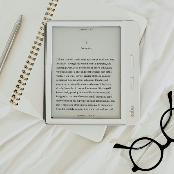 e-reader on top of a notebook with glasses in the bottom right corner