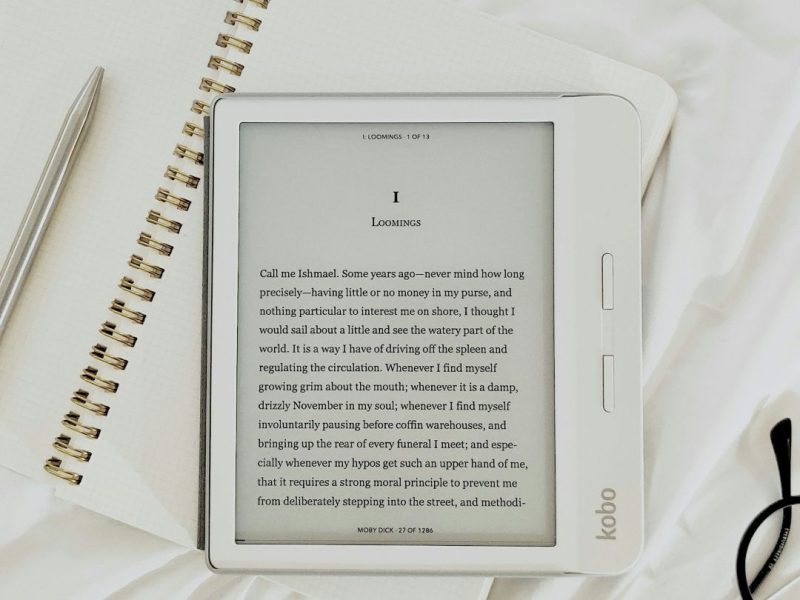 e-reader on top of a notebook with glasses in the bottom right corner