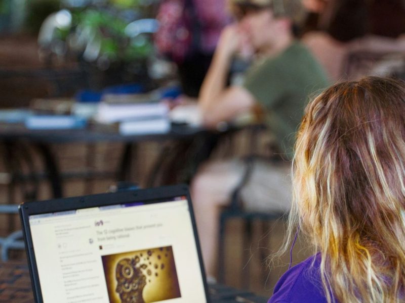 student reviewing course material on their laptop in a busy cafe area
