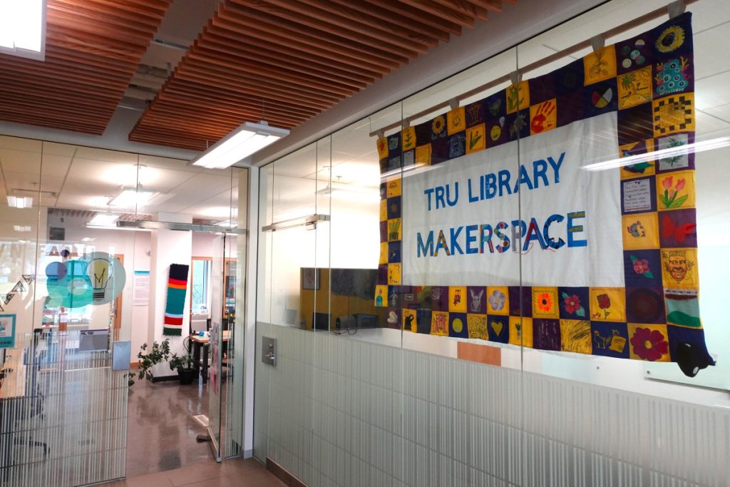 Collaborative banner that says TRU LIbrary Makerspace made up of individual fabric squares designed by the TRU community hung in the entrance to the Makerspace to the right of Tim Hortons.
